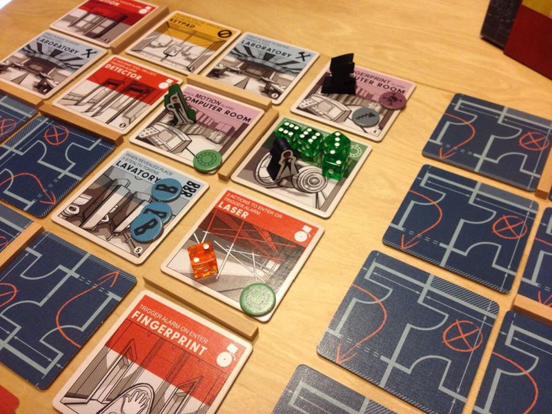 two groups of tiles featuring blueprints on one side and descriptions of rooms on the other.  several wooden tokens and dice are on a few of the tiles