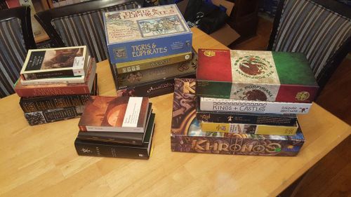 A pile of board games on a table. Titles include Tigris & Euphrates, Khronos, Kings & Castles, and more