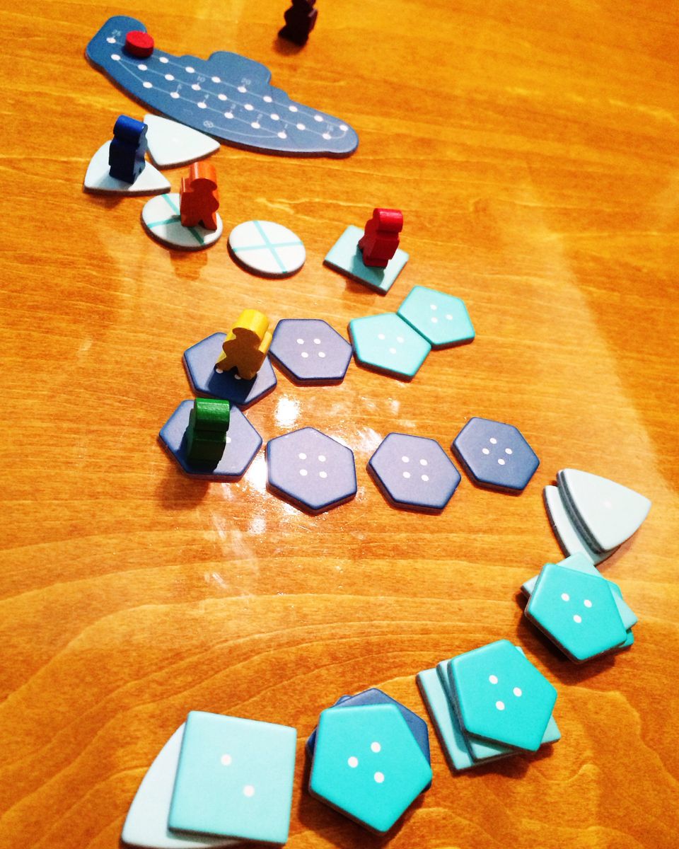 blue cardboard chits make a trail away from a cardboard submarine.  Several colorful divers have stopped at spots on the trail