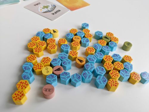 An array of wooden hex-shaped tokens including blue toy boxes and yellow pizzas